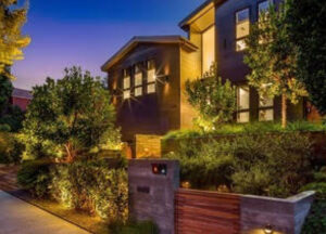 Beautiful suburban house with warm lighting and lush greenery at dusk.